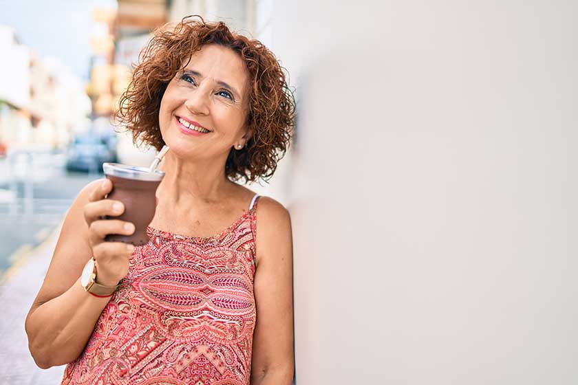 Middle age woman smiling happy leaning on the wall at street of city.